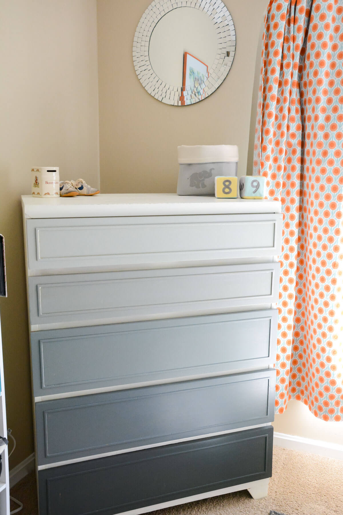 gray painted ombre dresser drawers with circle mirror on the wall.